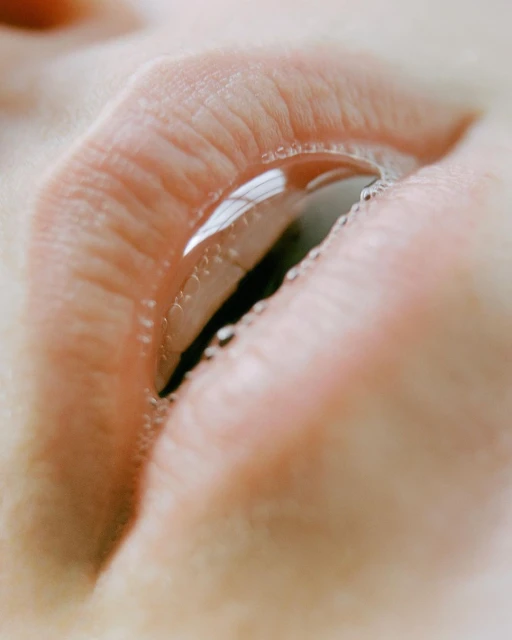 Close-up studio shot of a woman's lips with a transparent fluid or gel, highlighting skincare and beauty in a minimalist composition.