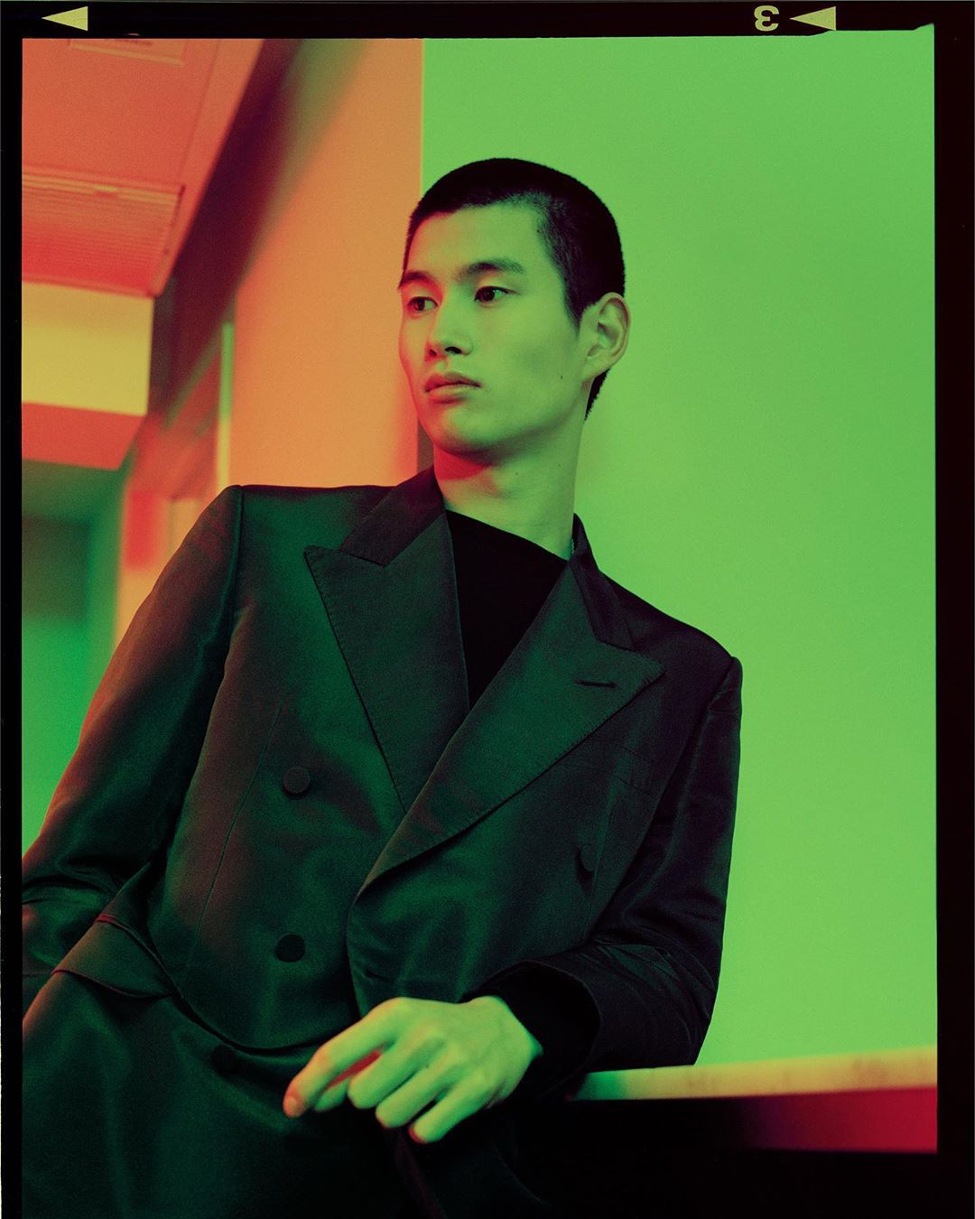 Portrait of a young Asian male model in a dark blazer and black shirt, shot with vivid orange and green lighting, emphasizing the clothing.