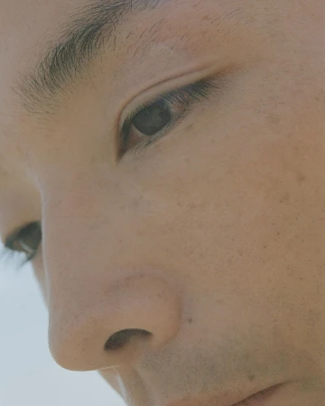 Extreme close-up portrait of a person's eye, nose, and cheek with natural skin texture and minimal makeup by Piczo.