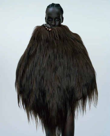 Portrait of a dark-skinned woman in a studio setting wearing a large, textured brown fur garment that covers most of her body.