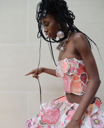 Black woman wearing a floral collage corset top and matching skirt with large silver earrings and braided hair