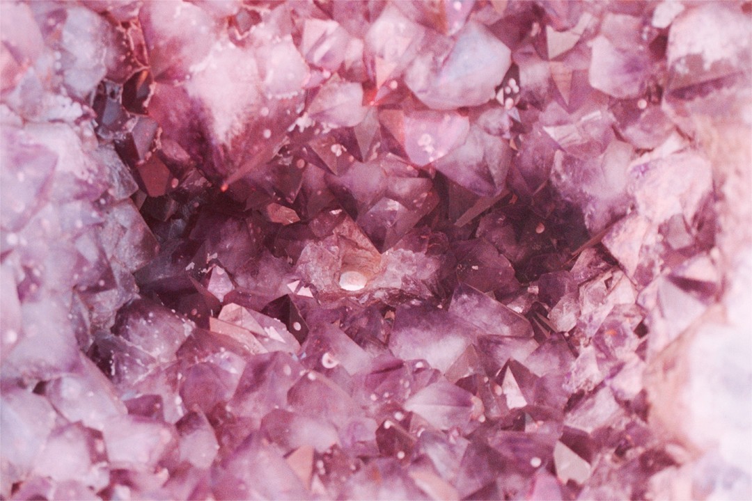 Macro photograph of an amethyst geode featuring crystal formations and a purple hue. Mineral specimen with detailed crystalline structure.
