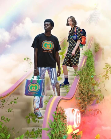 Two models pose on a pastel staircase with greenery. One carries a Gucci tote, wearing shiny pants and a Gucci logo t-shirt.