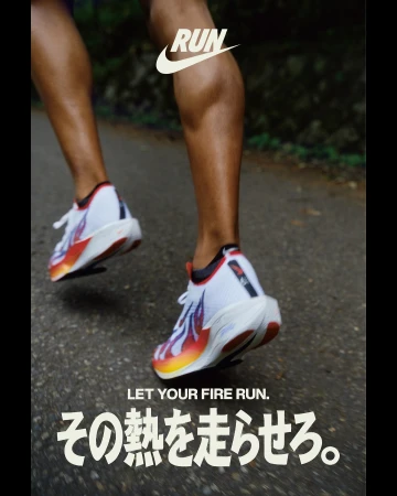 Runner's legs and feet in motion, featuring white and colorful running shoes with the Nike logo, on a gray asphalt road.