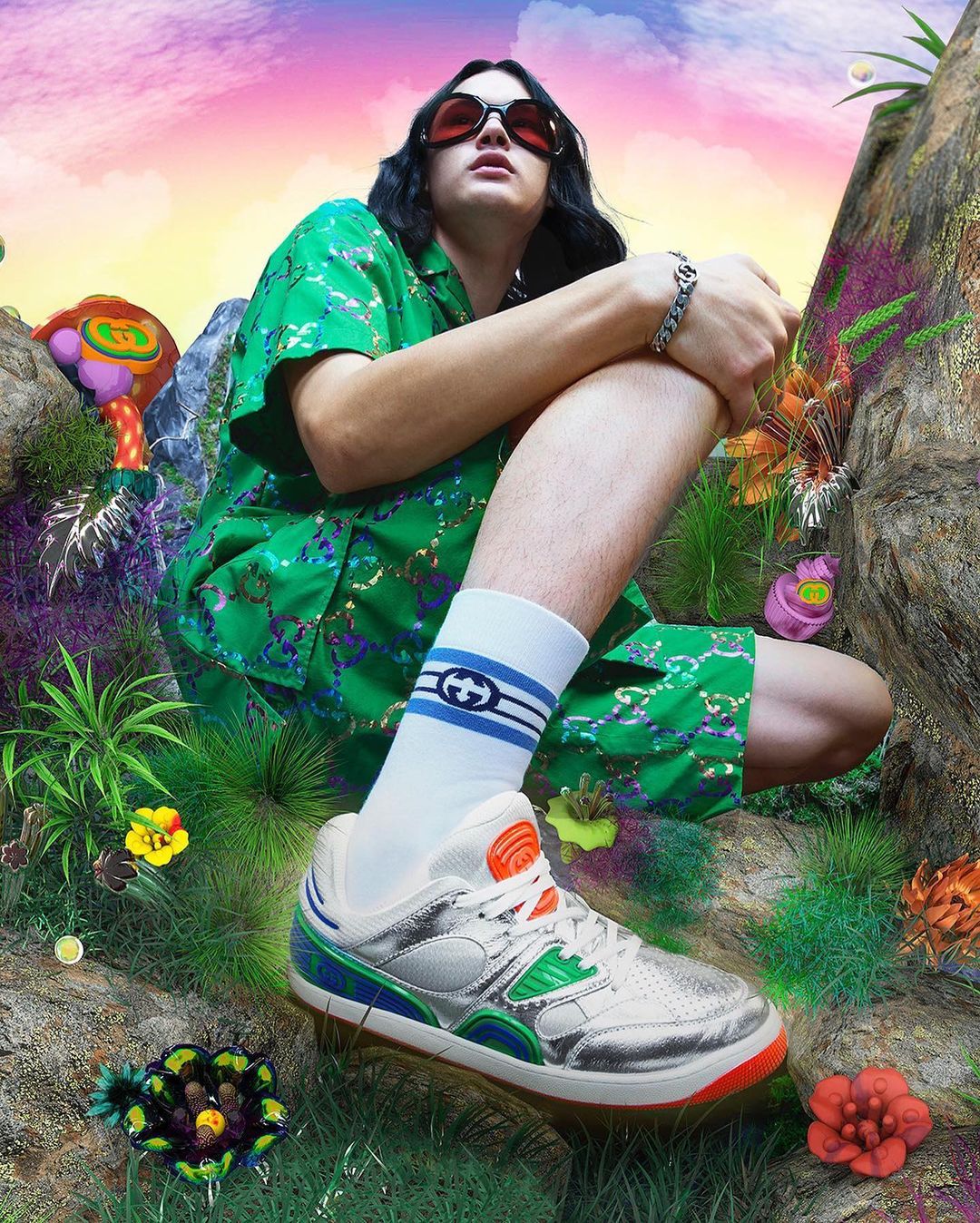 Person sits in a stylized, surreal outdoor scene showcasing a fashion sneaker, wearing a matching green patterned outfit and Gucci socks.