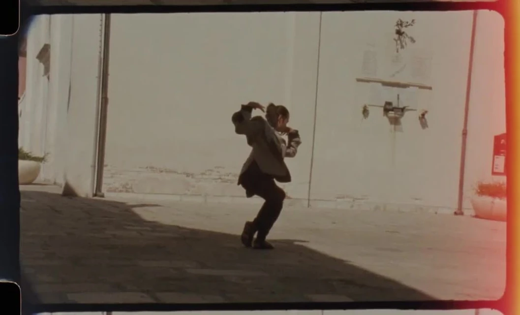Adult in business attire dancing outdoors, framed by buildings and open sky, capturing dynamic movement and urban setting.