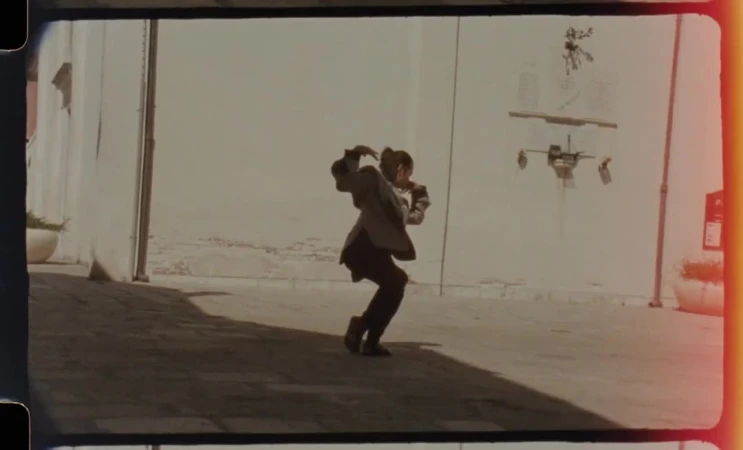 Adult in business attire dancing outdoors, framed by buildings and open sky, capturing dynamic movement and urban setting.