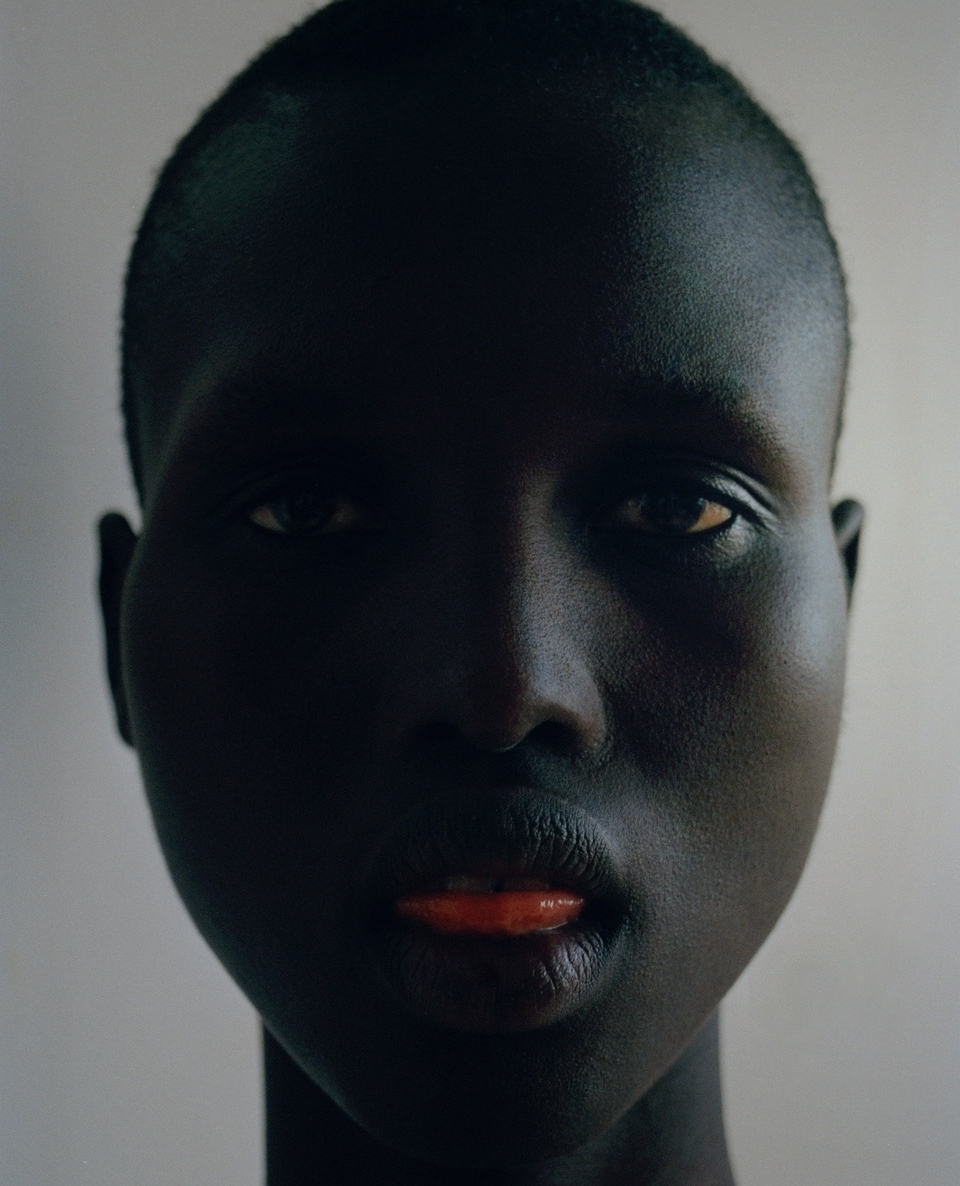 Striking close-up portrait of an African American woman with dark skin and orange lipstick, set against a neutral background.