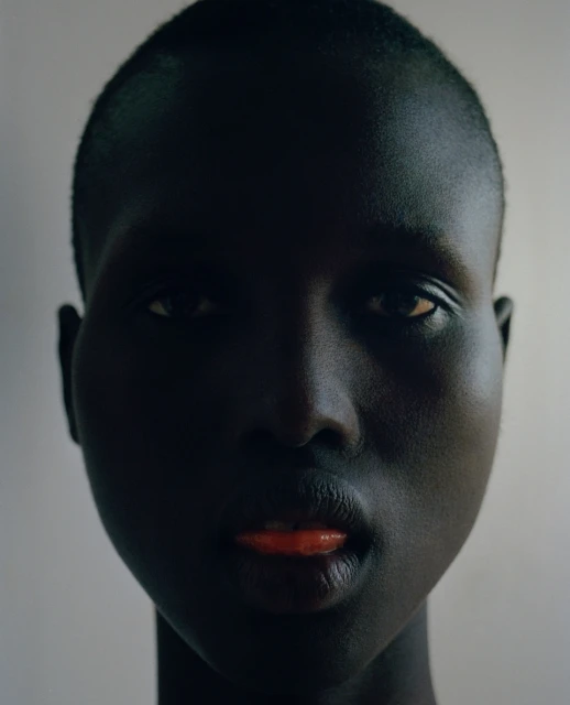 Striking close-up portrait of an African American woman with dark skin and orange lipstick, set against a neutral background.
