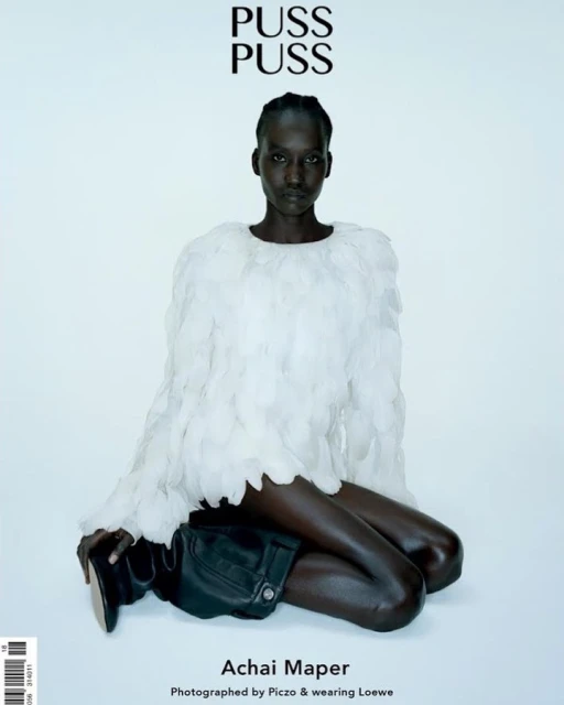 Fashion editorial shot of a dark-skinned model wearing a feather-like top and black boots against a light backdrop, magazine cover.