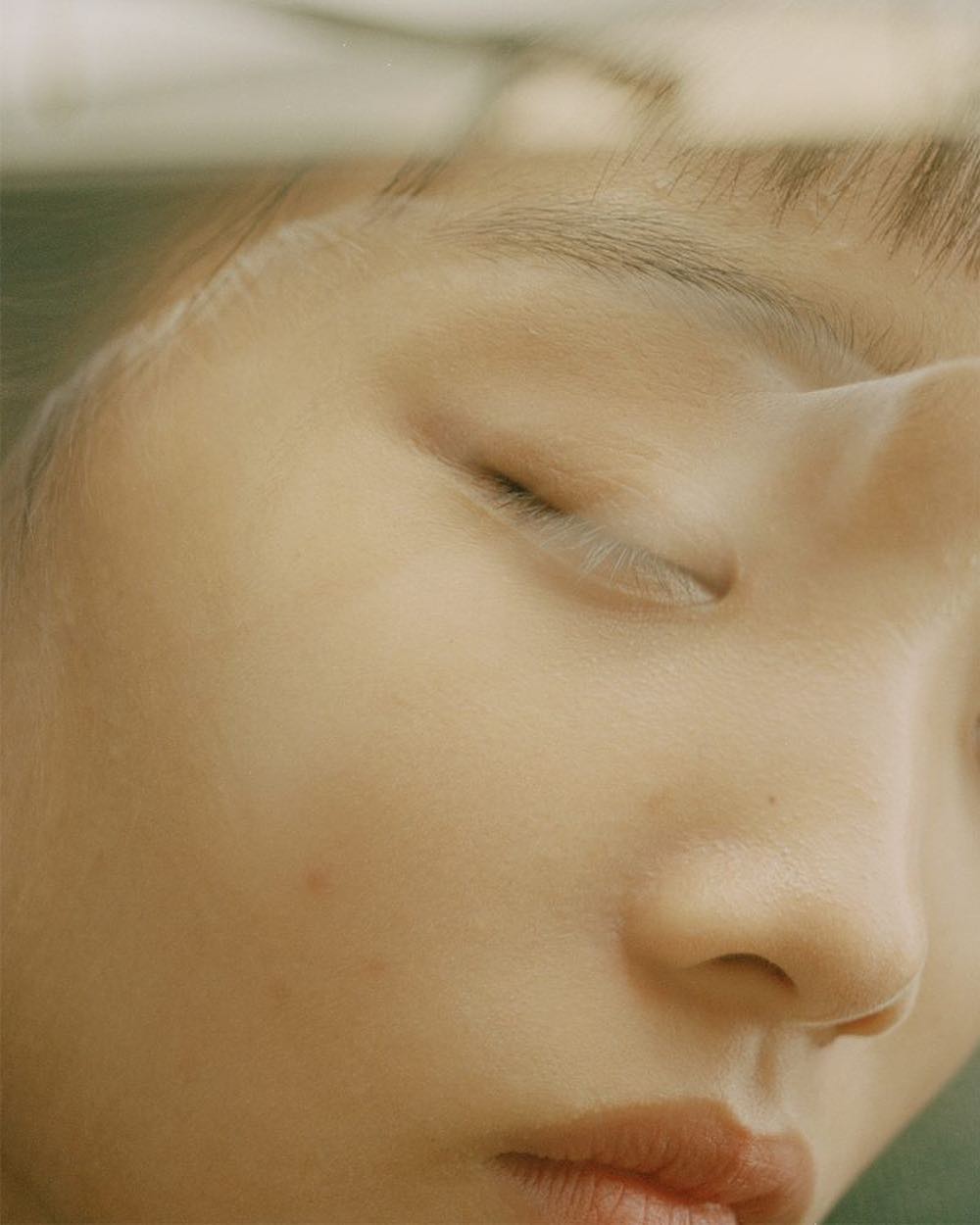 Close-up portrait of a young adult female with her eyes closed. Soft lighting highlights the woman's facial features in a bright, airy atmosphere.