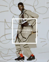 Black man wearing plaid suit and black sneakers with red socks against a backdrop with handwritten markings