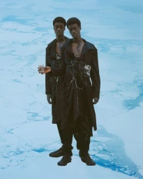 Two black men in dark coats standing on an icy blue frozen lake holding a glass