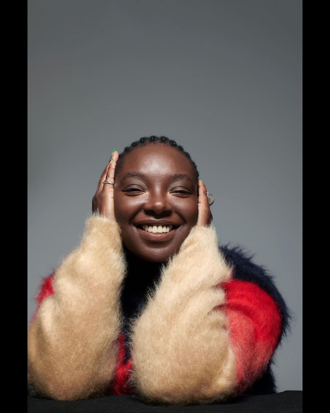 Smiling Black woman in a colourful sweater. Portrait of a cheerful African woman in fashion attire against a neutral grey background.