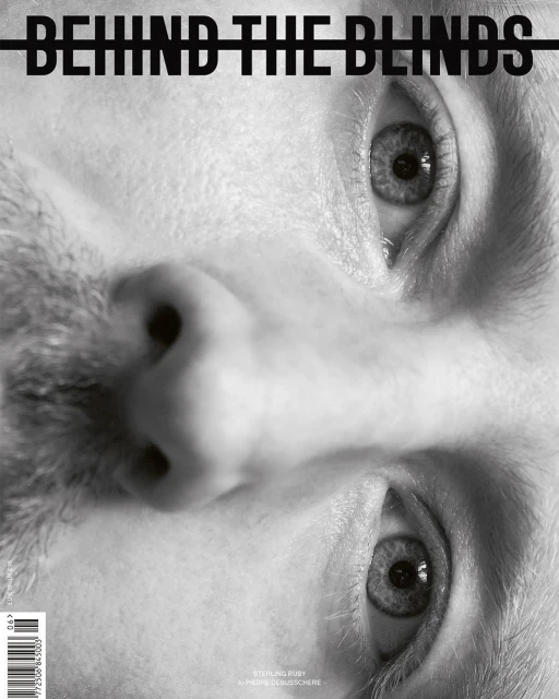Black and white close-up of a man's face, presented upside down, with a magazine title 'Behind the Blinds' overlaid.