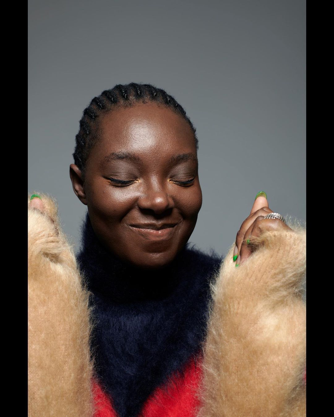Close-up studio portrait of a smiling African-American woman wearing a multicolored, high-neck sweater with fluffy sleeves.