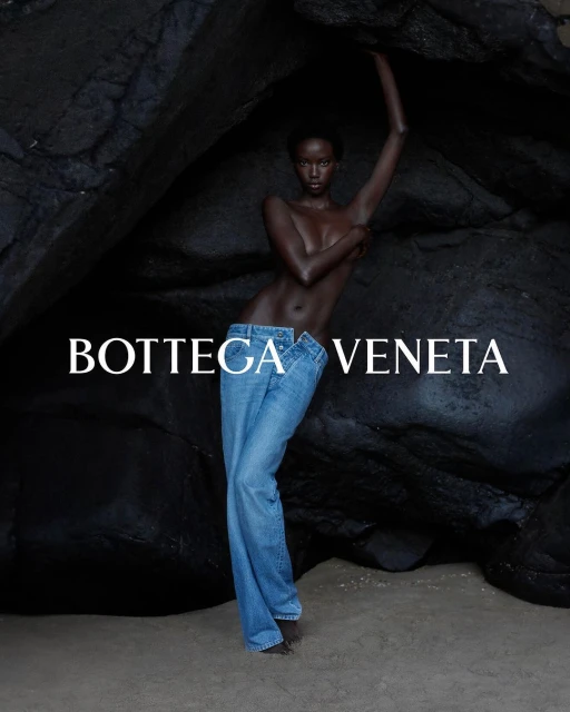 A woman posing in jeans against a rock formation, showcasing fashion, beauty, and editorial style with Bottega Veneta branding.