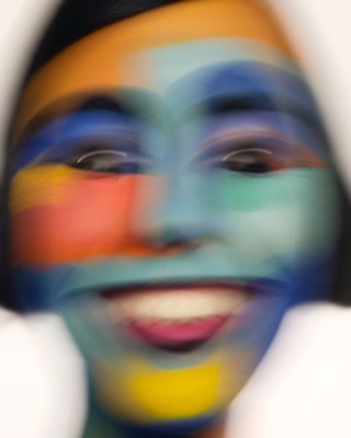 Artistic portrait of a woman with colorful face paint, smiling and exhibiting a vibrant and expressive style on a white backdrop.