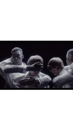 Four men in white shirts interacting closely against a dark background, captured by photographer Pierre Debusschere.