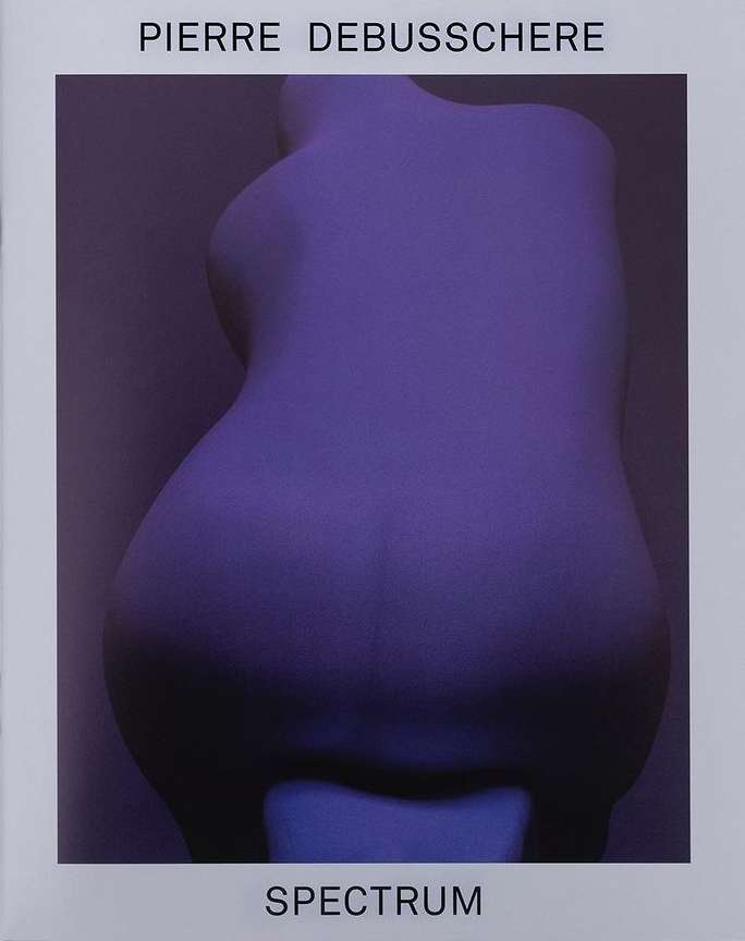 Back view of a female torso sculpture in a purple light against a purple background. Title text 'Spectrum' and artist name.