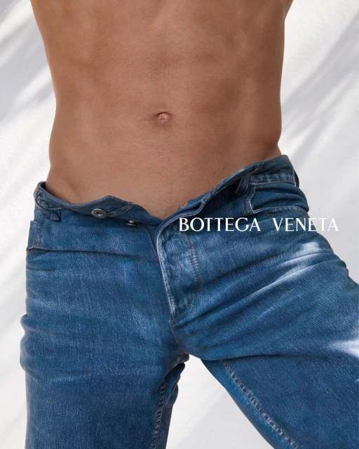 Mid-torso of a shirtless adult male in blue jeans against a neutral background with light, casting subtle shadows behind him.