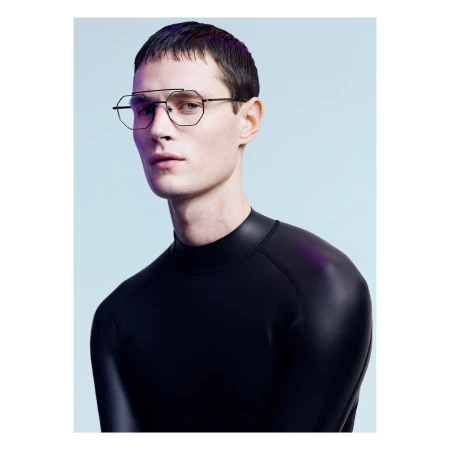 Close-up studio portrait of a young adult male model with short dark hair wearing geometric eyeglasses and a black mock turtleneck shirt.