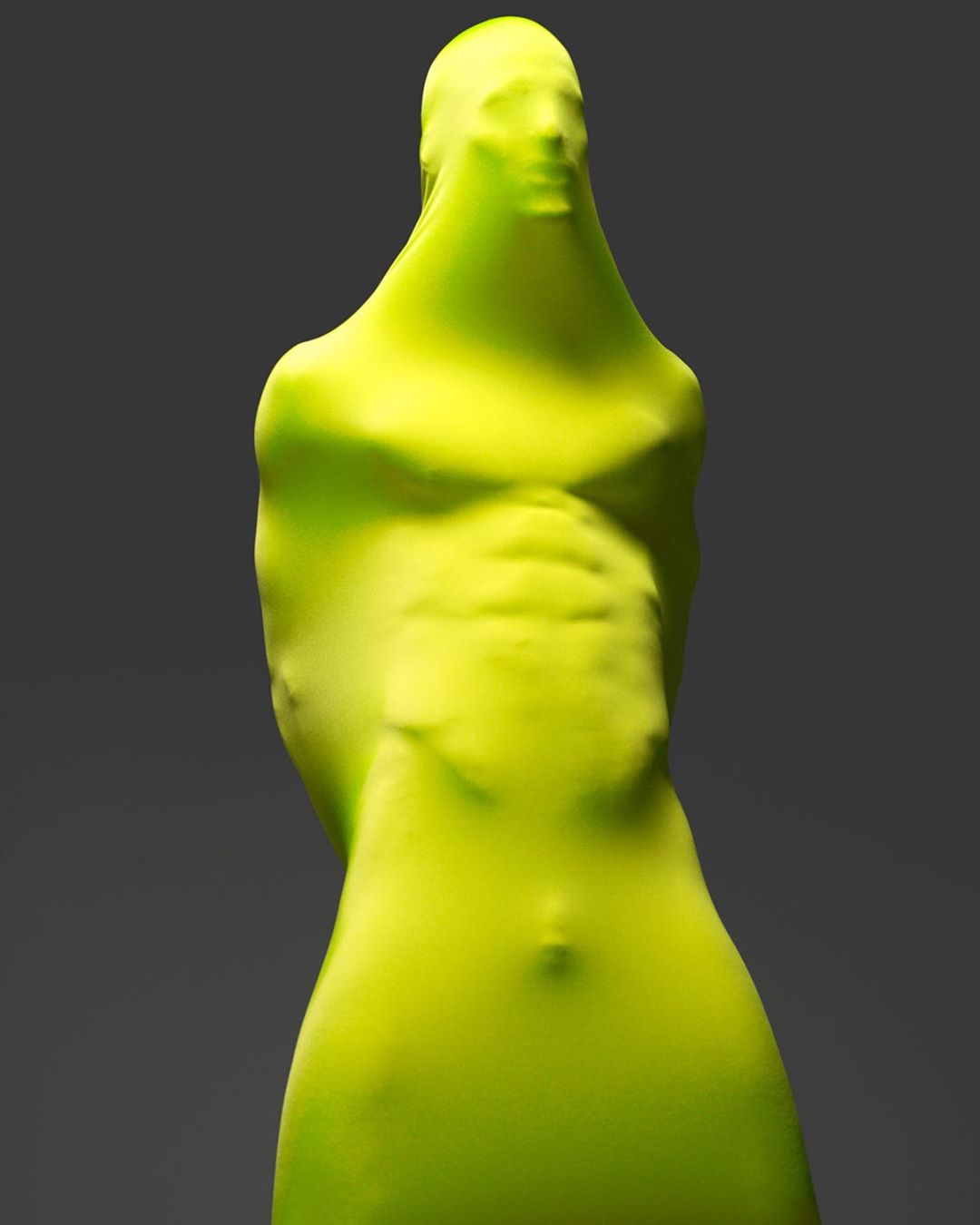 Abstract figure covered in chartreuse fabric standing against a grey background in a brightly lit studio environment.