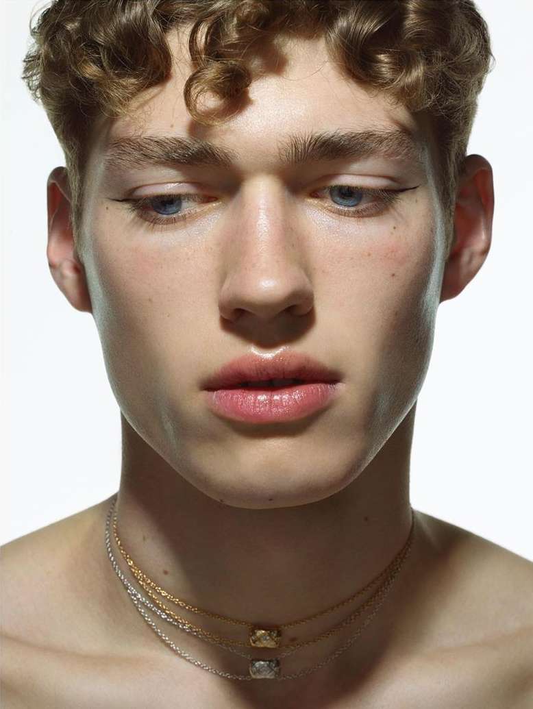 Close-up portrait of a young man wearing layered necklaces against a plain white background by Pierre Debusschere