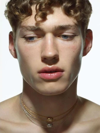 Close-up portrait of a young man wearing layered necklaces against a plain white background by Pierre Debusschere