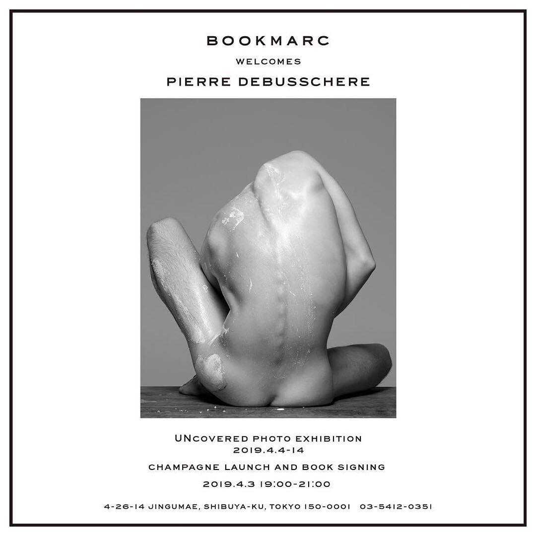 Black-and-white artistic nude portrait featuring a flexed adult male on a wooden surface, presented in a promotional poster for a photo exhibition.