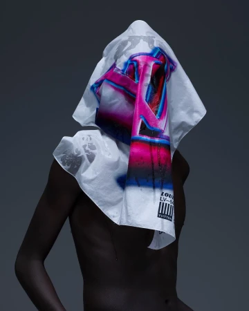 Person draped in a white Louis Vuitton printed textile, back to the camera in a studio setting with neutral grey background.
