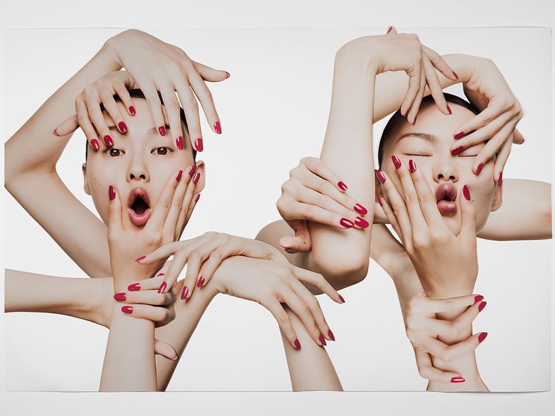 Two Asian women frame their faces with hands in a beauty shot, displaying red manicured nails against a clean white background.