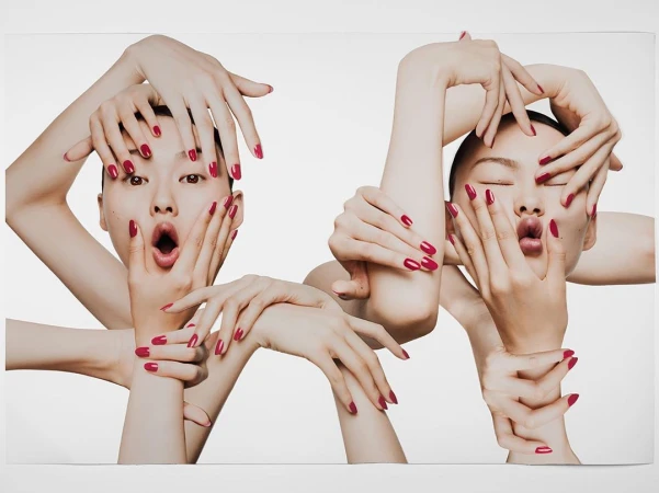 Two Asian women frame their faces with hands in a beauty shot, displaying red manicured nails against a clean white background.