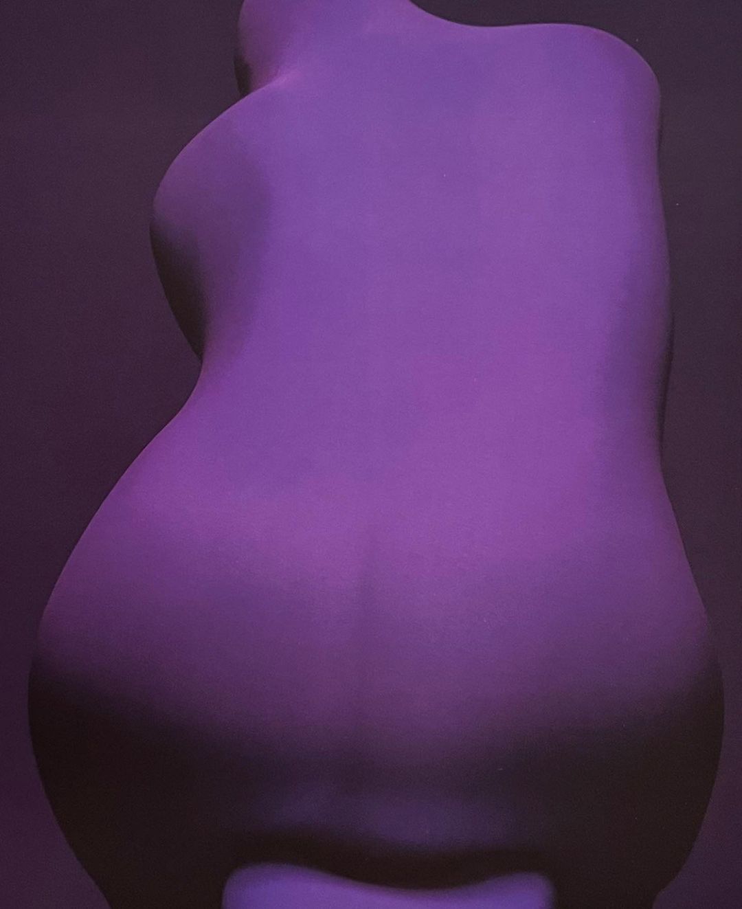 Abstract image of a purple mannequin torso against a gray background with studio lighting emphasizing the form and curvature of the object.