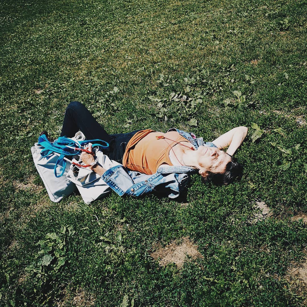 Woman lying on grass in sunlight with a denim jacket and bag. Casual clothing, relaxation and outdoor activity in a park-like setting.