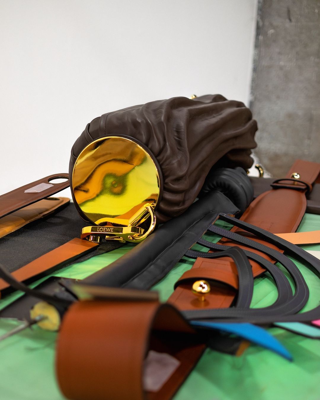 Loewe handbag displayed with leather crafting materials on a green surface, showcasing fashion accessories and craftsmanship.