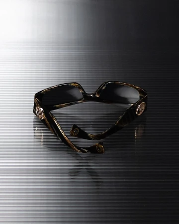 Tortoiseshell sunglasses with gold circular hardware resting on a ribbed grey metallic surface.