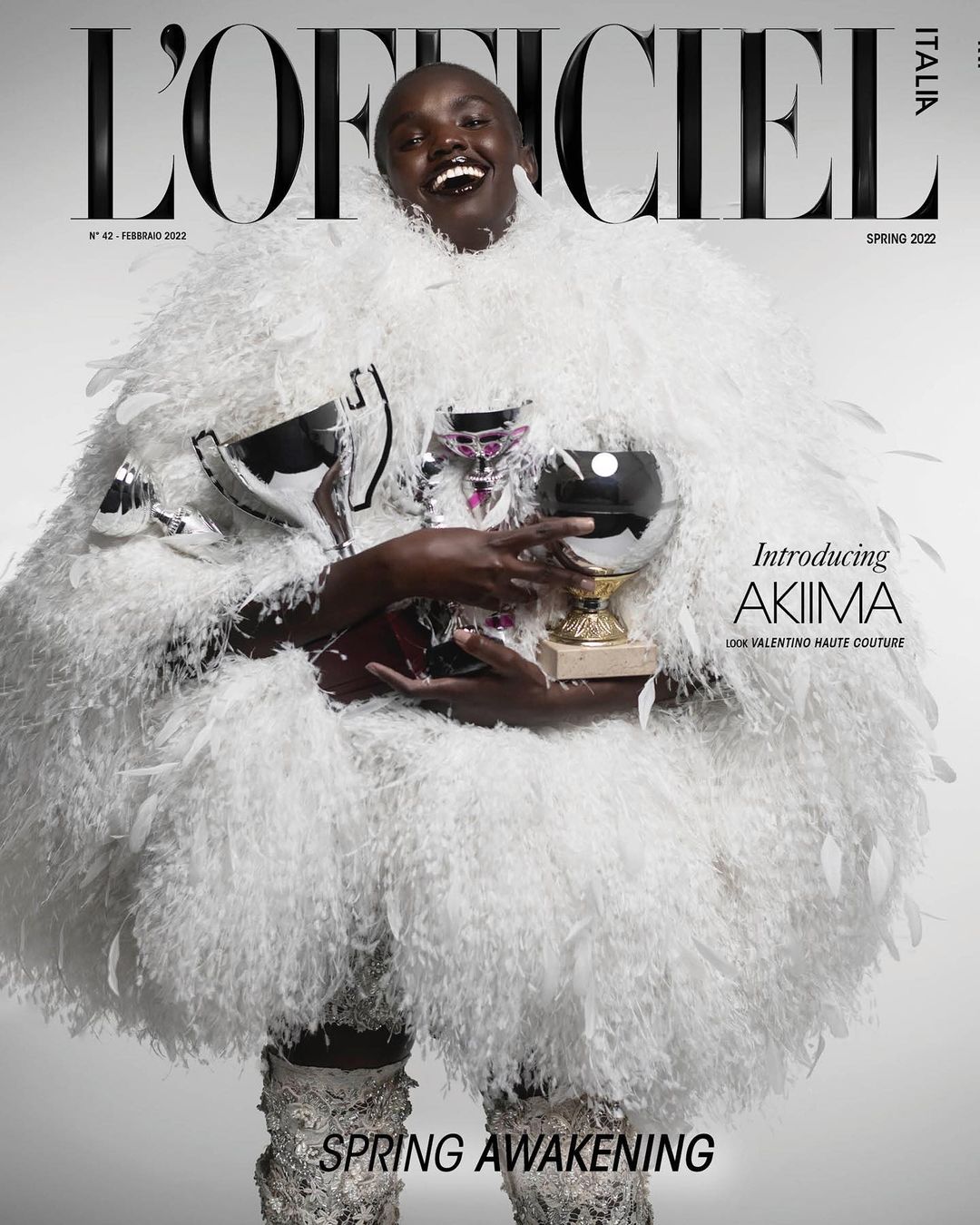 Magazine cover of a dark-skinned woman in a feather coat holding trophies, on a pale background with the 'L'Officiel Italia' masthead.