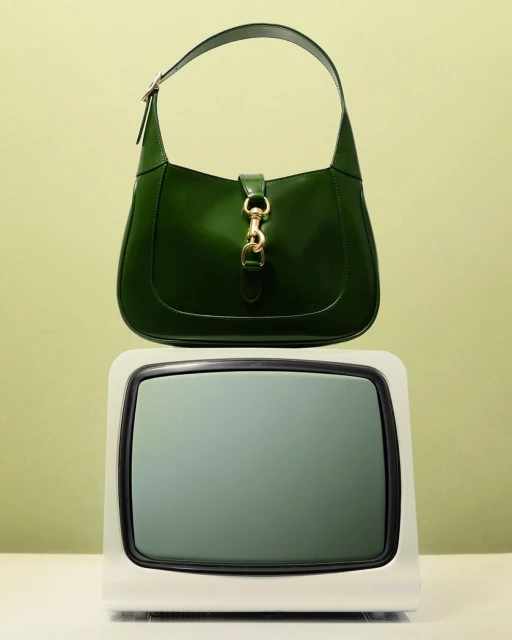 Green Gucci Jackie 1961 handbag is centered atop a white television against a light-green backdrop in a studio setting.