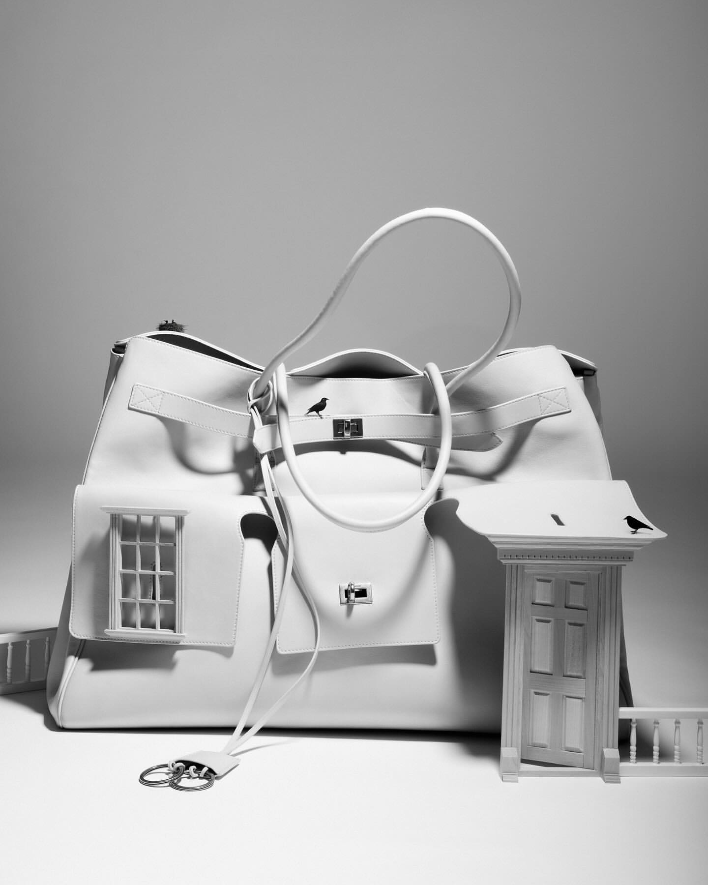 Conceptual fashion shot: An off-white leather satchel styled as a house with a window and door, set against a neutral background.