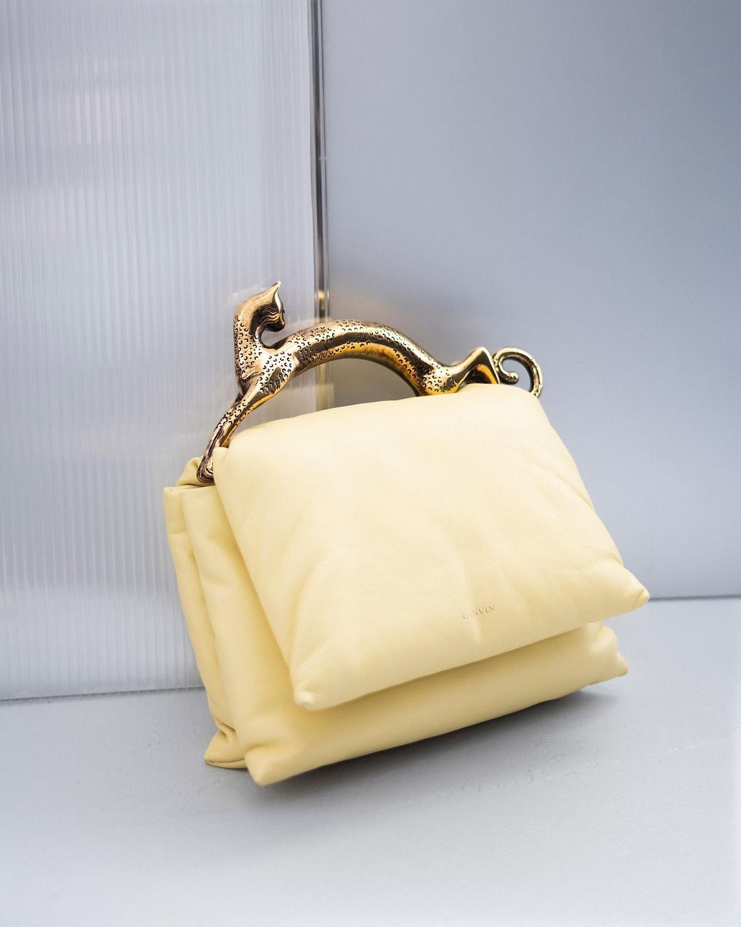 Elegant ivory-colored handbag featuring a unique gold panther handle, displayed against a softly lit, neutral background, fashion accessory.