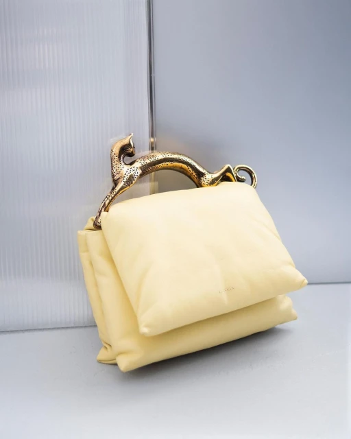 Elegant ivory-colored handbag featuring a unique gold panther handle, displayed against a softly lit, neutral background, fashion accessory.