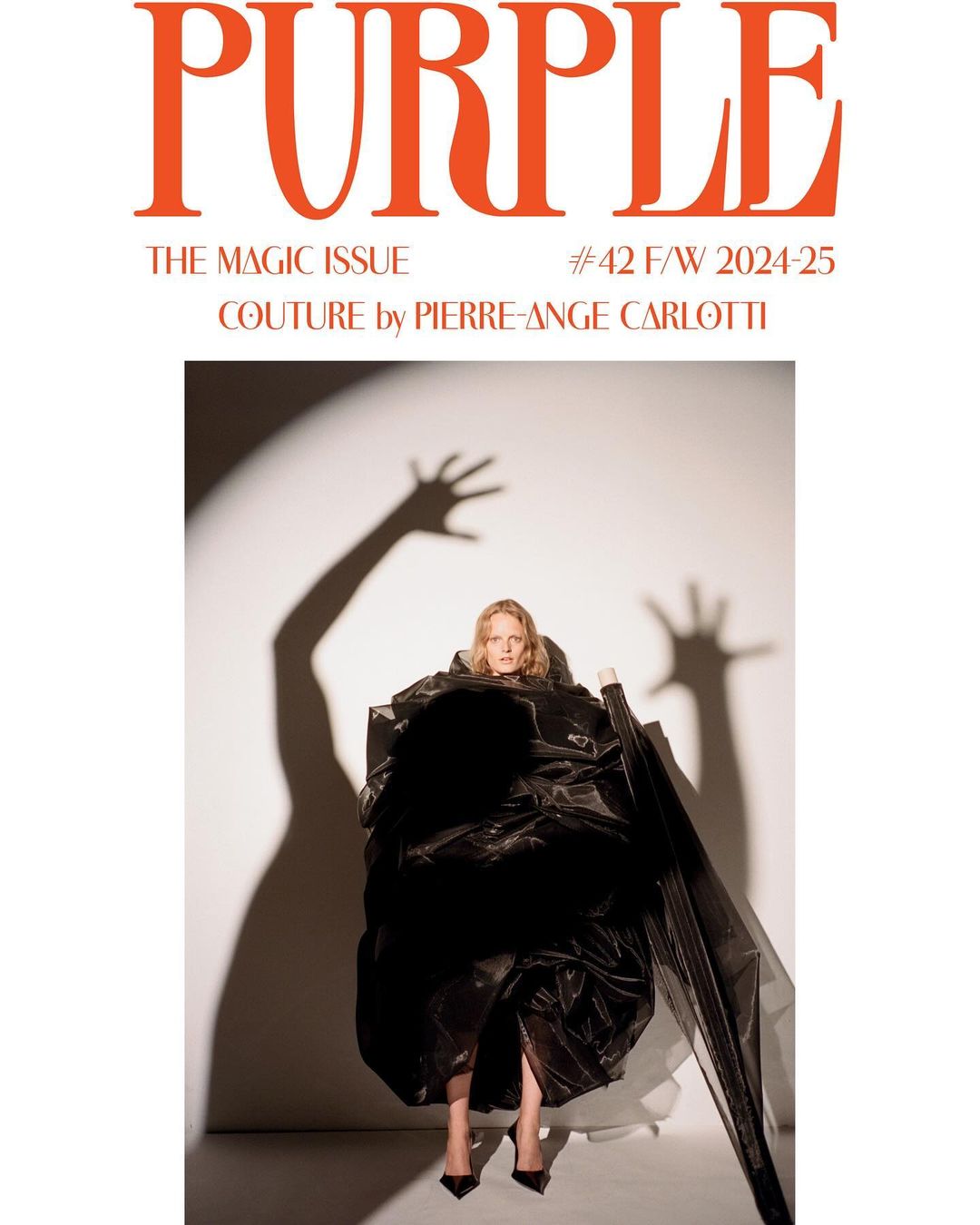 Blonde woman in a voluminous black dress poses for the cover of Purple Magazine's Magic Issue against a white backdrop with shadow art.