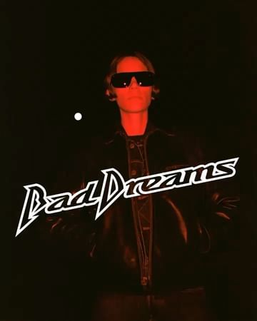 Person with sunglasses and jacket against dark red backdrop with text overlay. Low-key lighting and urban fashion aesthetic.