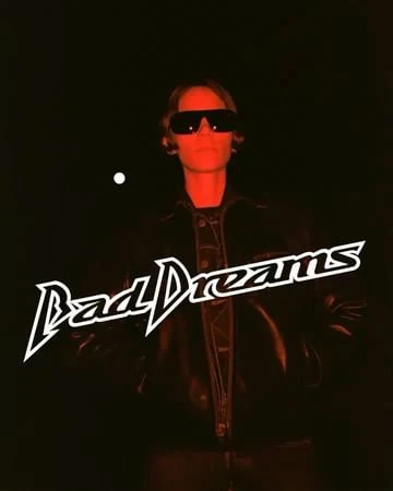 Person with sunglasses and jacket against dark red backdrop with text overlay. Low-key lighting and urban fashion aesthetic.