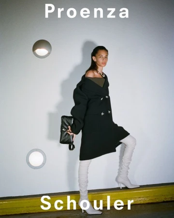 Fashion model poses against a white wall in a black coat, light-colored boots, and holds a black clutch. Proenza Schouler text is visible.