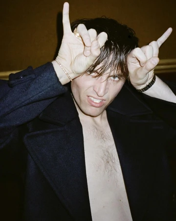 Man making hand horns gesture while wearing an unbuttoned dark coat in Paris by Pierre-ange Carlotti