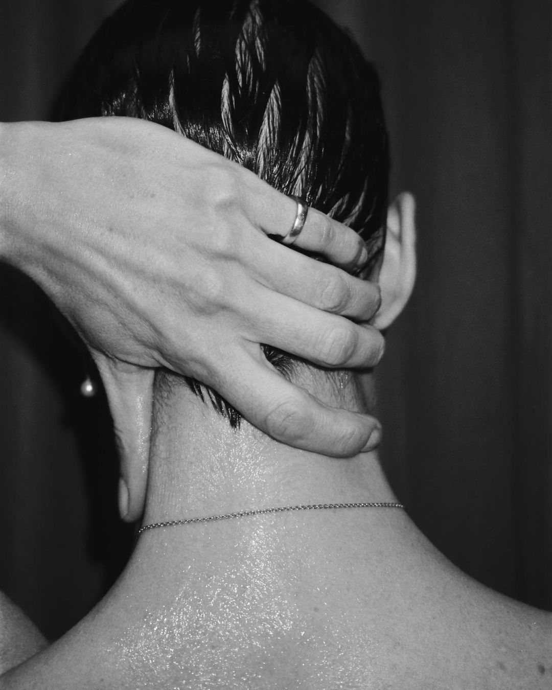 Close-up black and white shot of a person having their head massaged, showing an adult hand with a ring and a chain necklace.