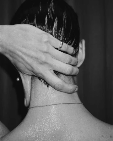 Close-up black and white shot of a person having their head massaged, showing an adult hand with a ring and a chain necklace.