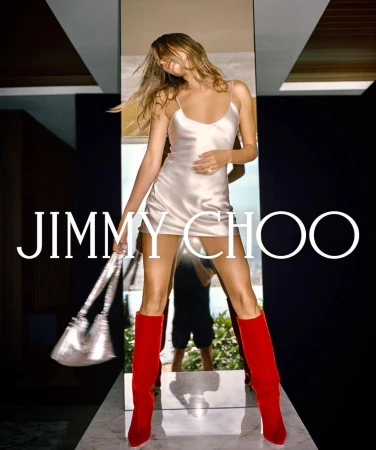 A woman poses in a champagne-colored dress, silver purse, and red boots, highlighted by the Jimmy Choo logo and indoor setting.